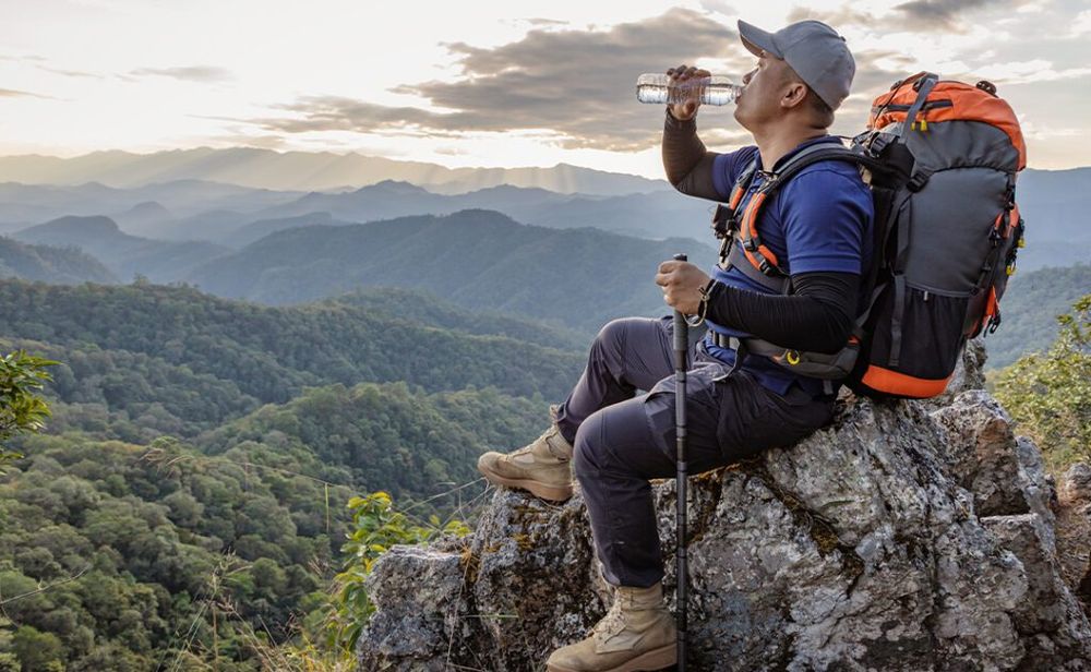 Hiker with backpack relaxing on top of the mountain and drinking bottled water